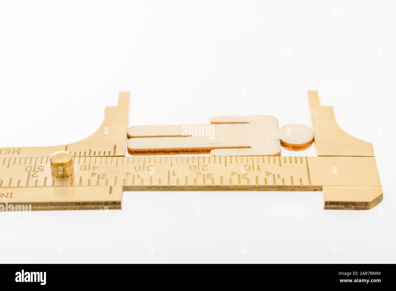 Makro kleine lasergeschnittene Holzfigur und Messing-Zirkel gegen den weißlichen BG. Messung von persönlichen Leistungsindikatoren, demografischen Daten, Produktivität, Stockfoto