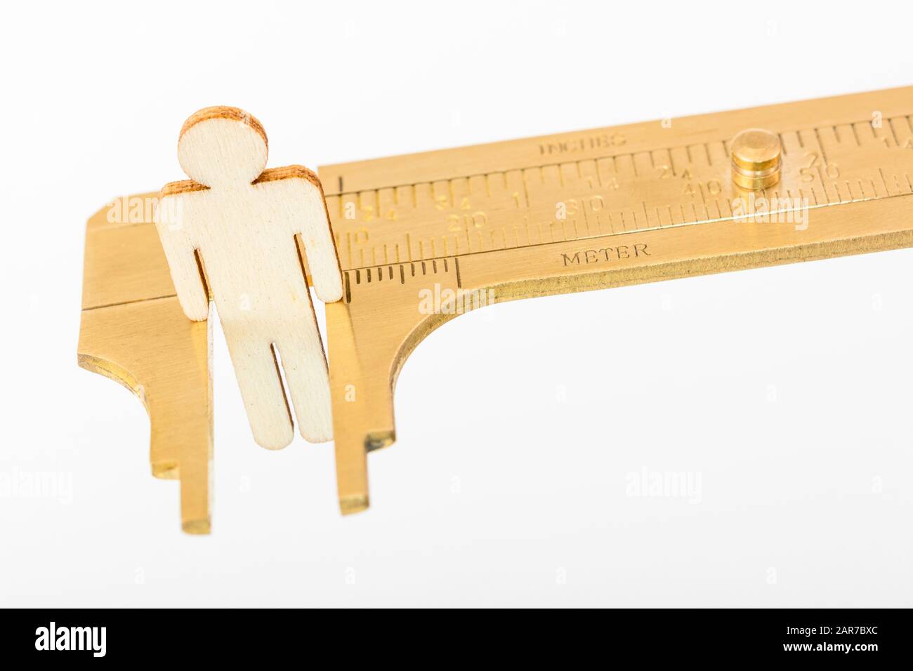 Makro kleine lasergeschnittene Holzfigur und Messing-Zirkel gegen den weißlichen BG. Messung von persönlichen Leistungsindikatoren, demografischen Daten, Produktivität, Stockfoto