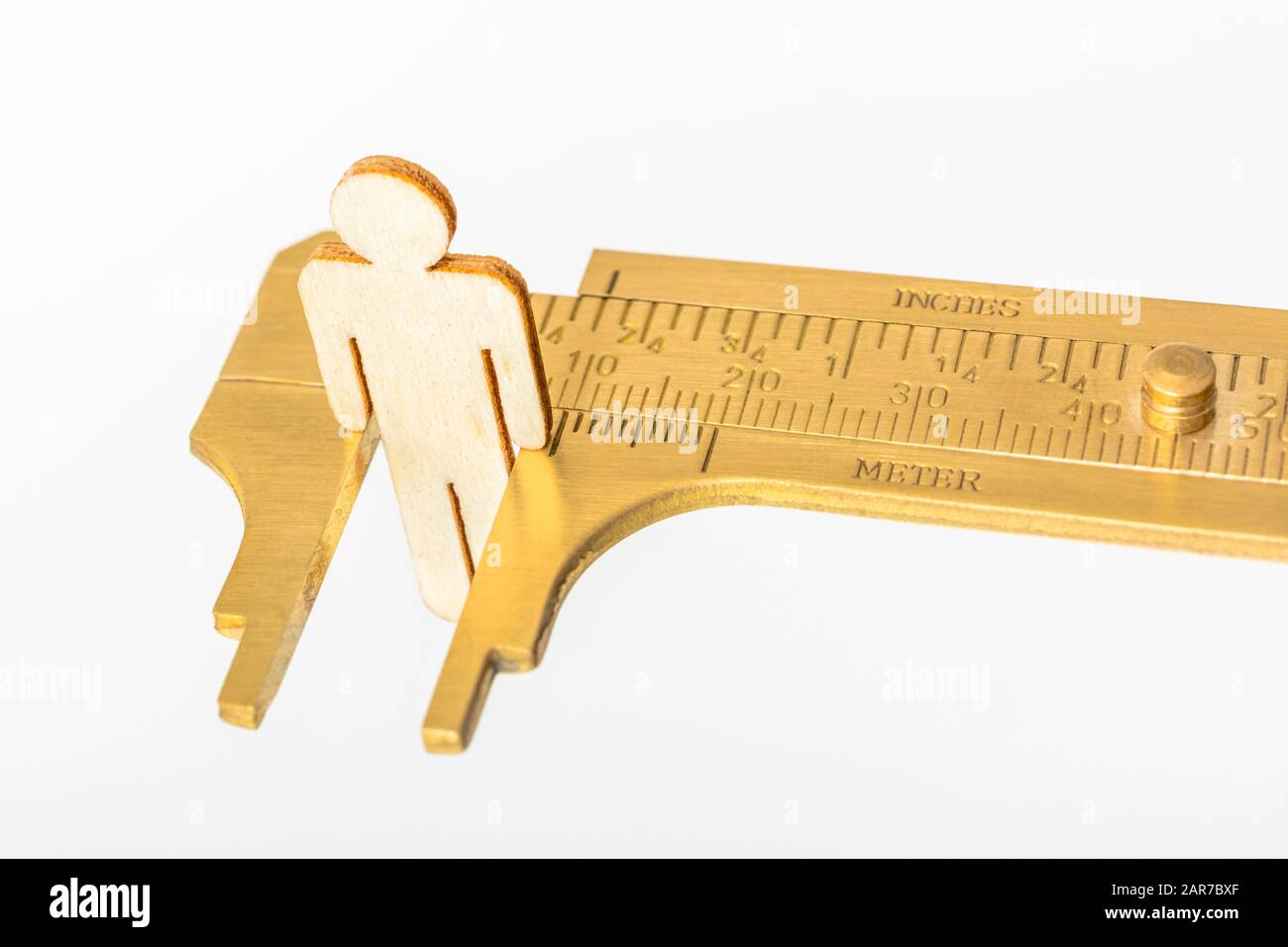 Makro kleine lasergeschnittene Holzfigur und Messing-Zirkel gegen den weißlichen BG. Messung von persönlichen Leistungsindikatoren, demografischen Daten, Produktivität, Stockfoto