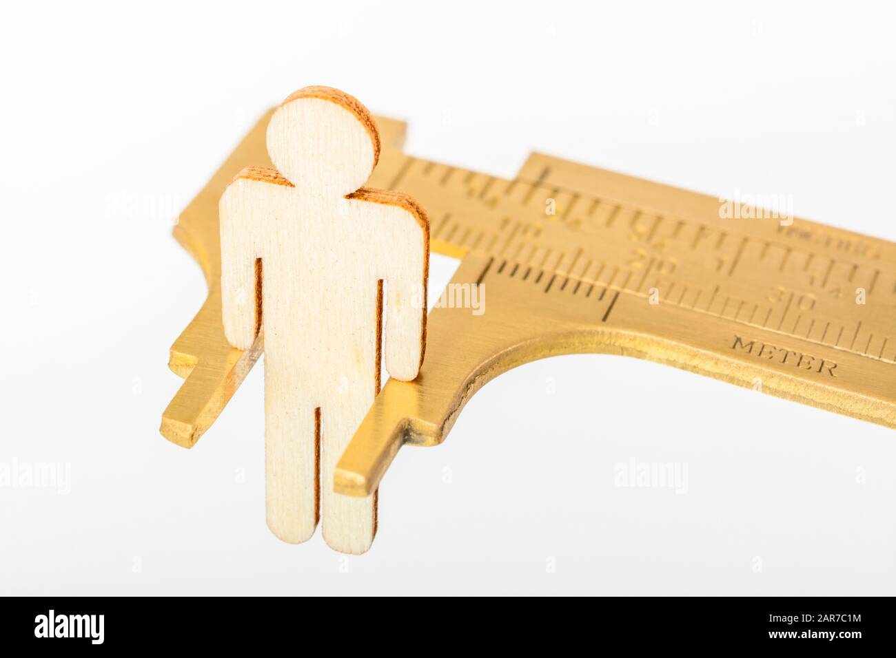 Makro kleine lasergeschnittene Holzfigur und Messing-Zirkel gegen den weißlichen BG. Messung von persönlichen Leistungsindikatoren, demografischen Daten, Produktivität, Stockfoto