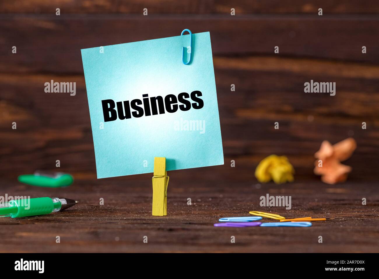 Karte mit der Aufschrift "Business" am Clip befestigt. Holzhintergrund, zerknitterte Papierkugeln, Büroklammern und ein Stift. Entwicklungskonzept Stockfoto