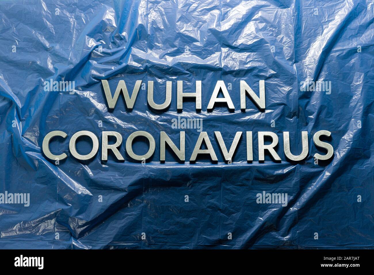 Wörter wuhan coronavirus gelegt mit Metallbuchstaben auf zerknittertem Blau Kunststoff-Folie Hintergrund - flach legen mit Komposition Stockfoto