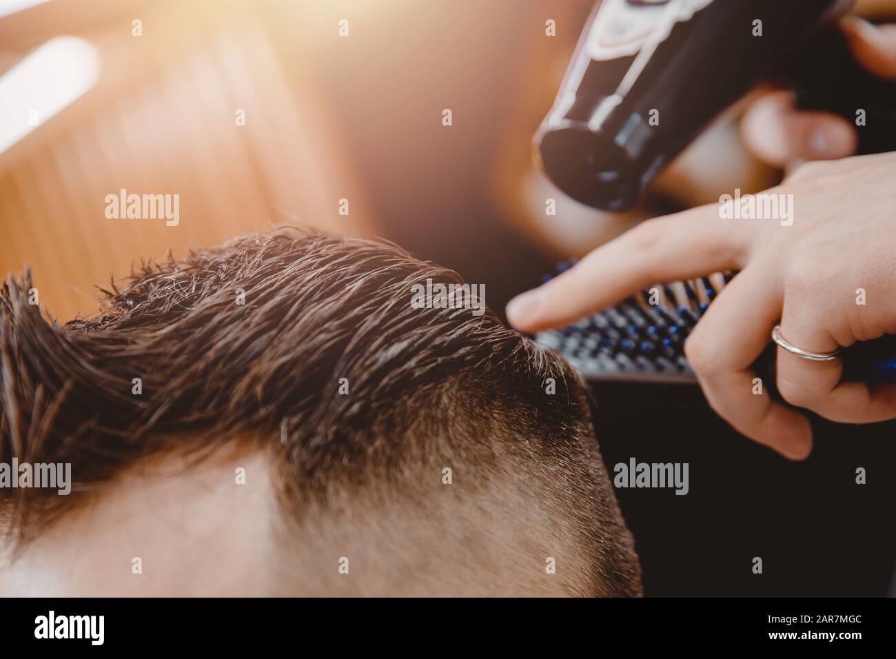 Der Masterstylist bringt den Mann mit Haarfön und Kamm, Modebarbershop, mit Haaren in die Haut Stockfoto