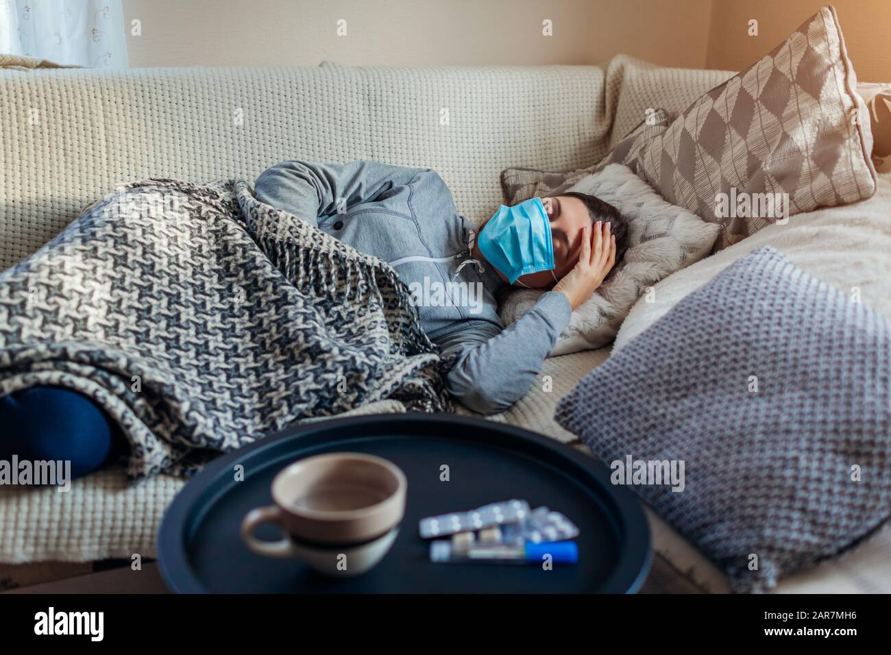 Kranke Frau mit Grippe oder Erkältung. Mädchen im Bett liegend, mit Schutzmaske durch Pillen und Wasser auf dem Tisch Stockfoto