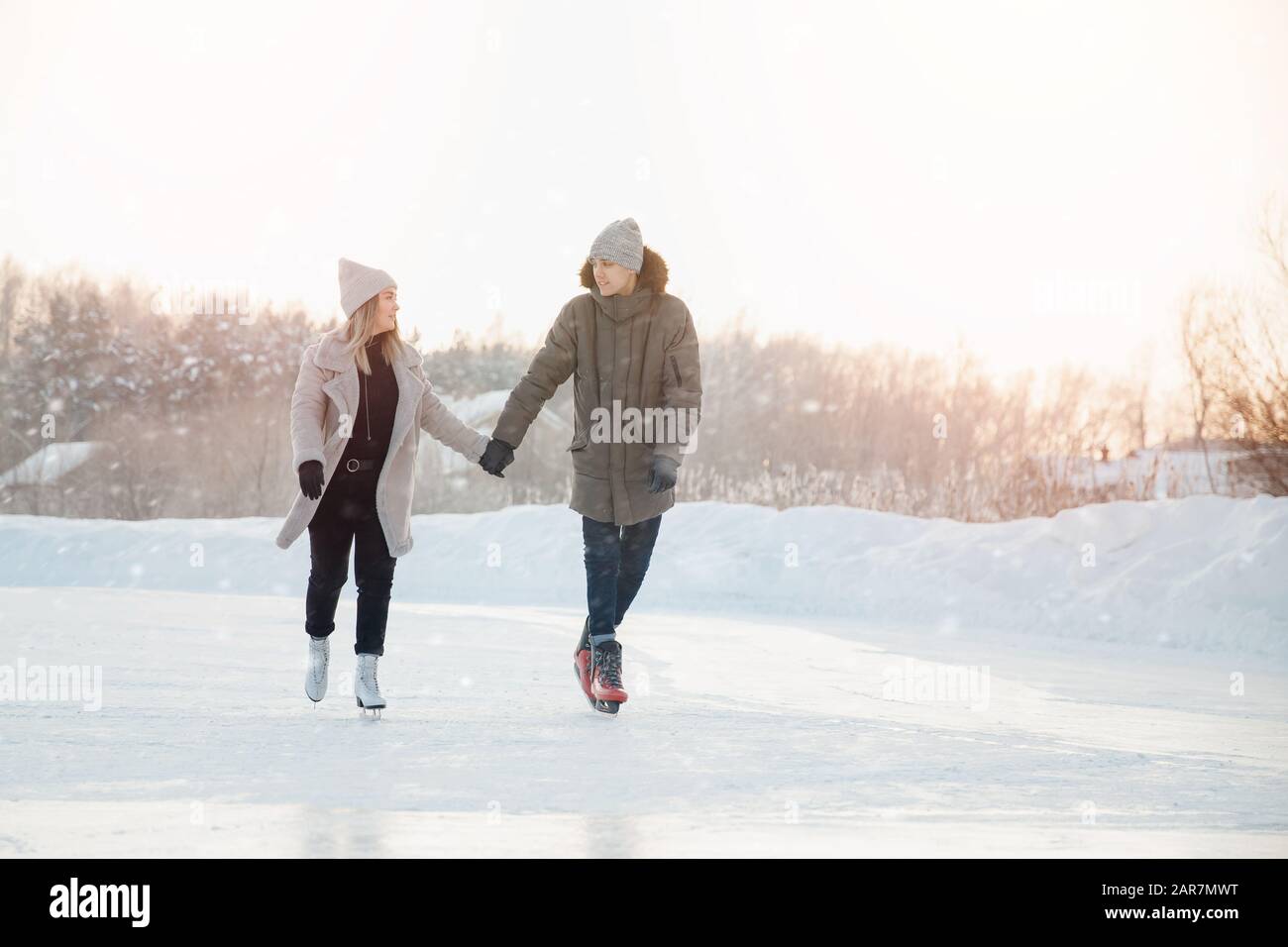 Mädchen und Mann halten sich die Hände, die sich gegenseitig blicken und essen auf gefrorenem Eis des Sees auf Schlittschuhen. Im Hintergrund ist Sonnenuntergang Stockfoto