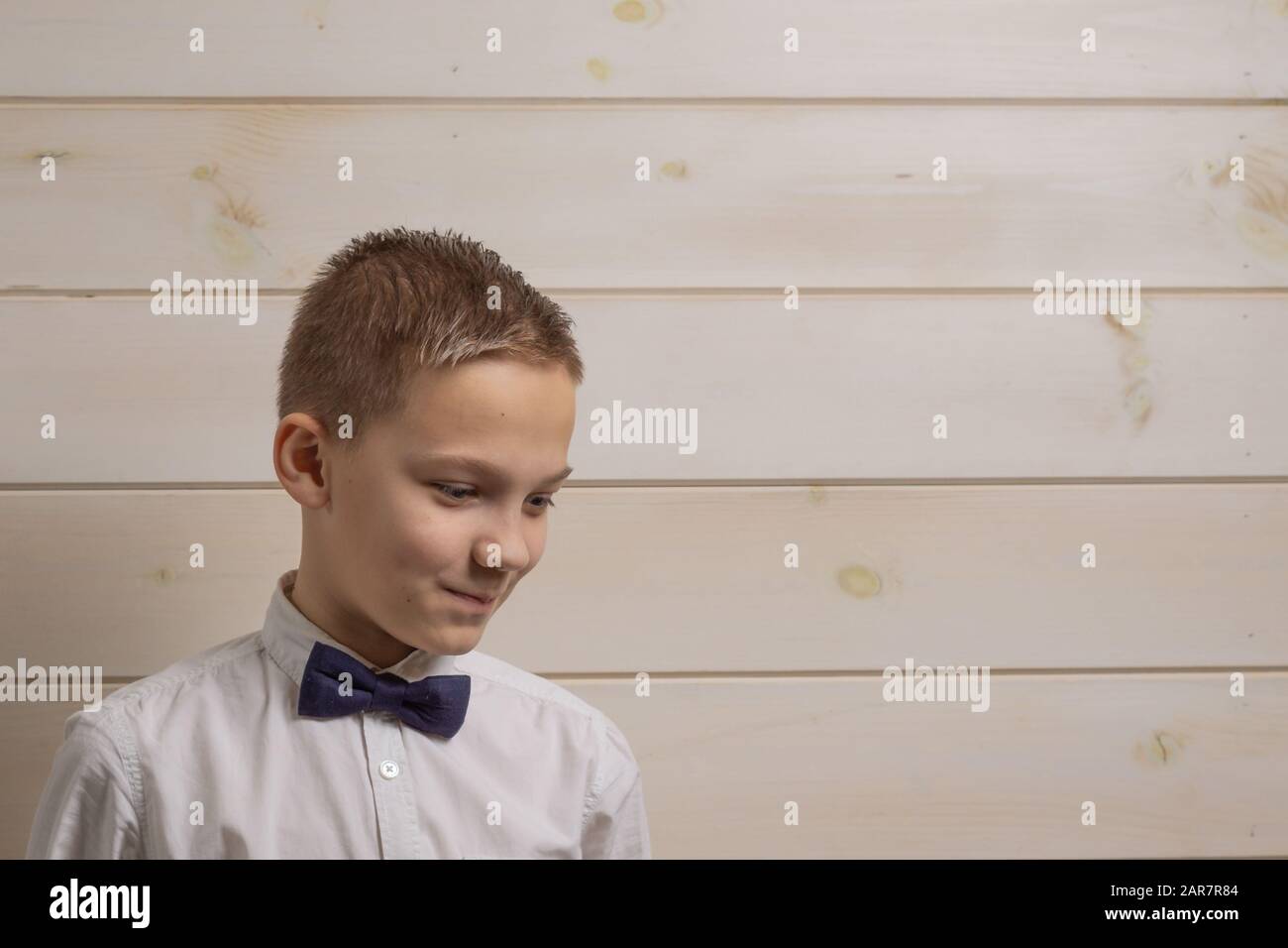 Ein zehnjähriger fadenhaariger Junge in einem weißen Hemd mit der selbstbinderigen Bow Tie lächelt vor dem Hintergrund einer Holzwand Stockfoto