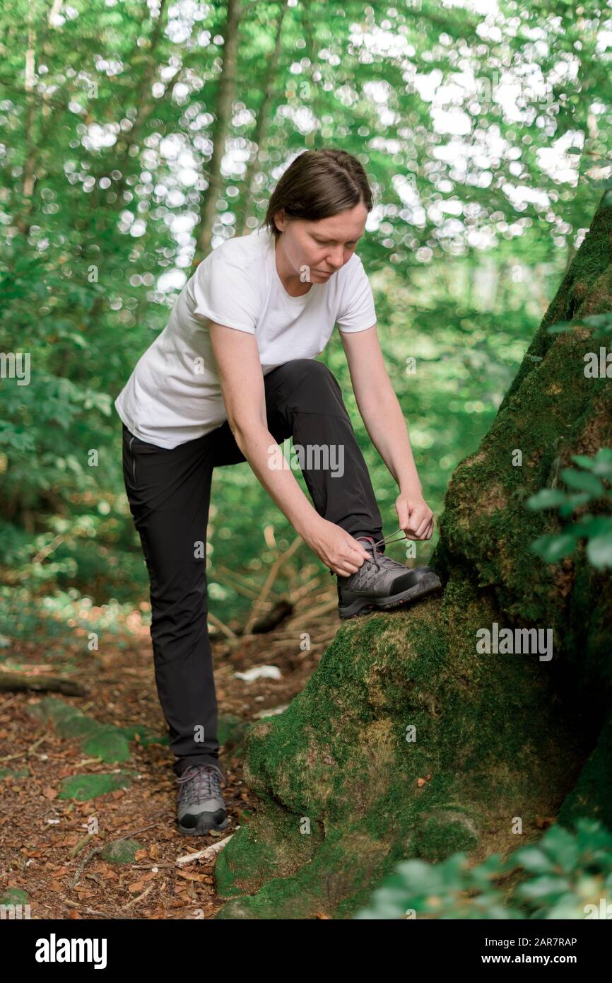 Weibliche Wanderer, die Schnürsenkel in Wald binden, während sie im Freien wandern, geringe Schärfentiefe, selektiver Fokus Stockfoto