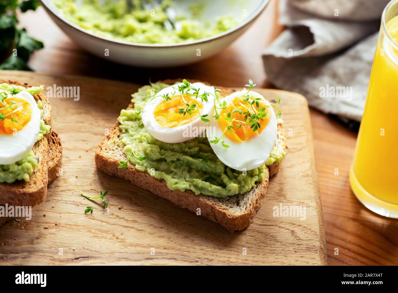 Toast mit Avocado und gekochtem Ei, garniert mit Mikrogrüns auf einem Holztisch. Gesundes Frühstück Stockfoto