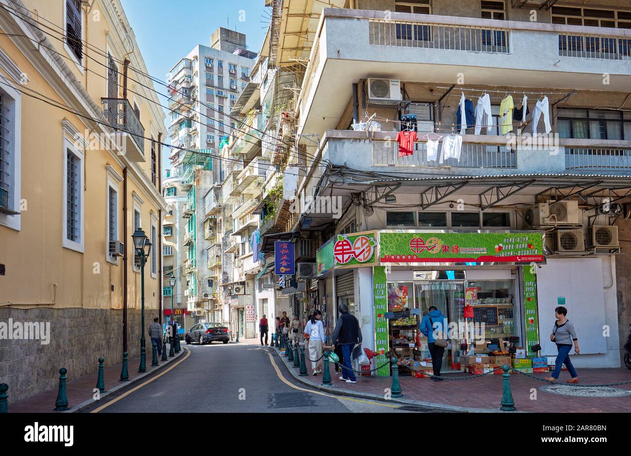 Menschen, die auf einem schmalen Bürgersteig im historischen Zentrum von Macau, China, spazieren gehen. Stockfoto