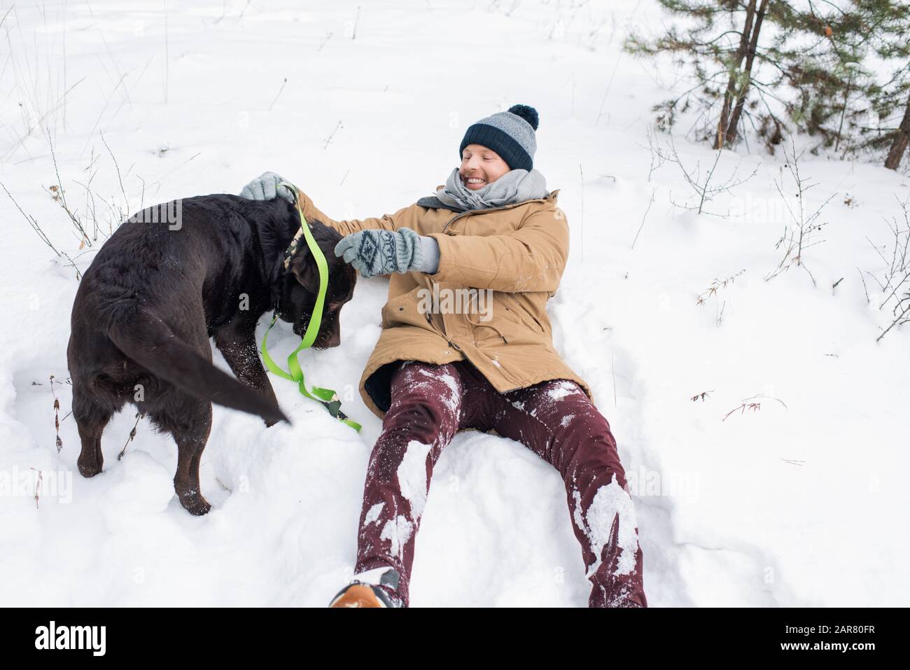 Fröhlicher Kerl im Winter, der Spaß beim Spielen mit schwarzem Retriever im Schnee hat Stockfoto
