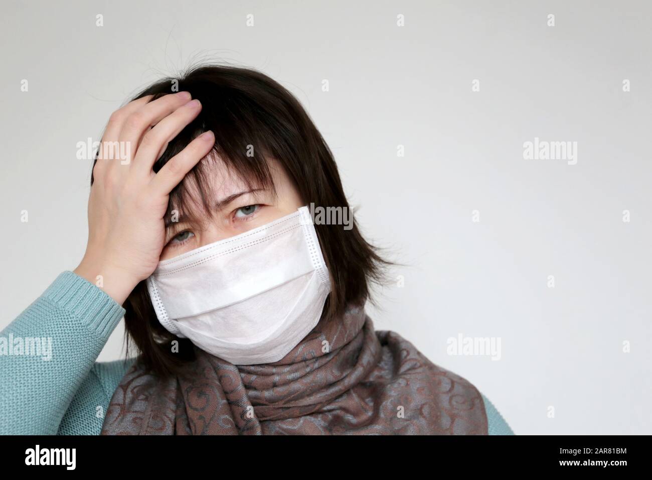 Unglückliche Frau in medizinischer Maske hält die Hand an der Stirn. Konzept von Krankheit, Fieber, Kälte und Grippe, Kopfschmerzen, Coronavirus-Symptome Stockfoto