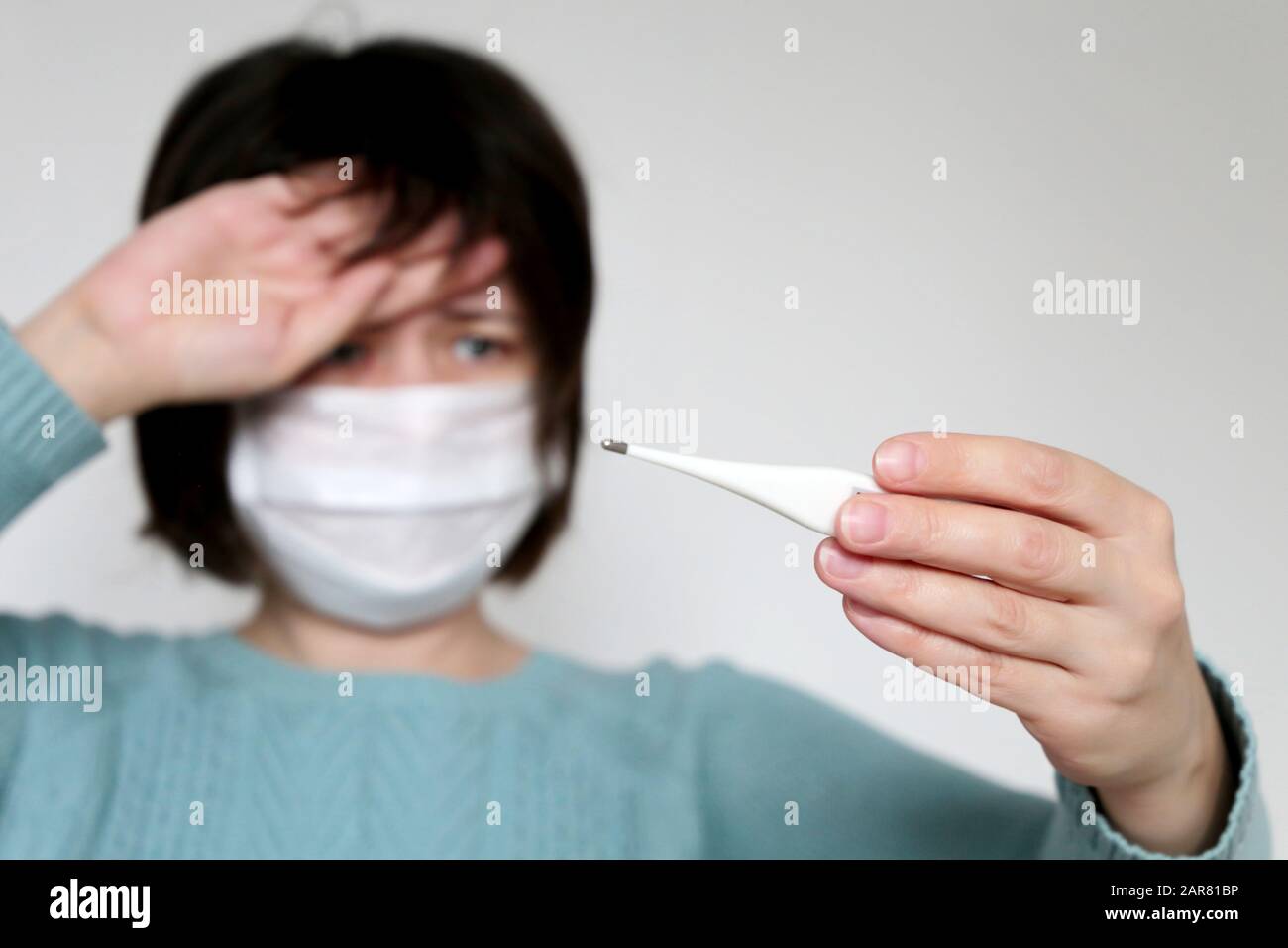 Die Frau in der medizinischen Maske misst die Körpertemperatur. Das kranke Mädchen betrachtet das Digitalthermometer in ihren Händen, das Konzept von Erkältung und Grippe, Fieber und Coronavirus Stockfoto