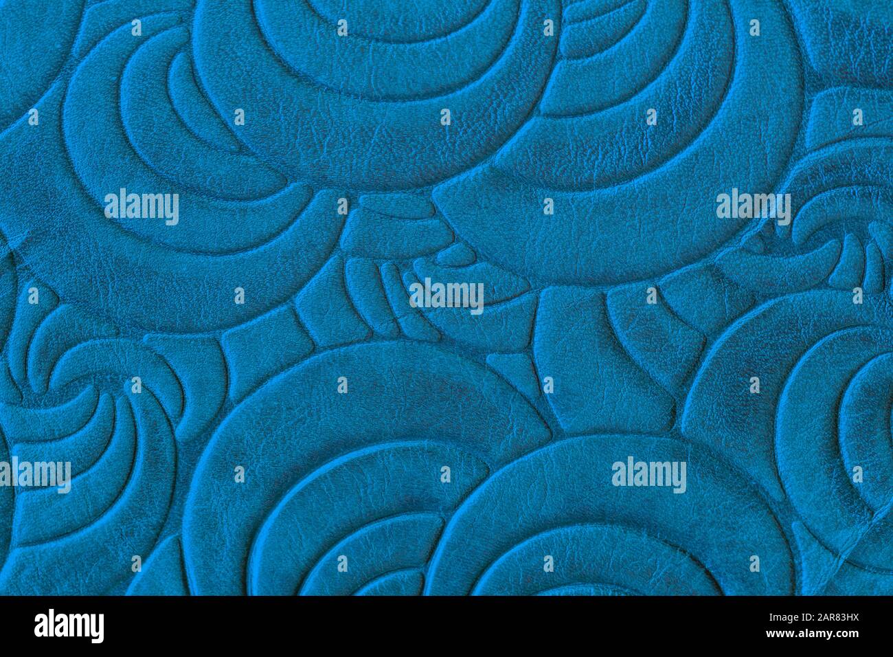 Textur aus blauem echtem Leder in Nahaufnahme, mit eingeprägtem spiralförmigem Trendmuster. Modischer Hintergrund Stockfoto