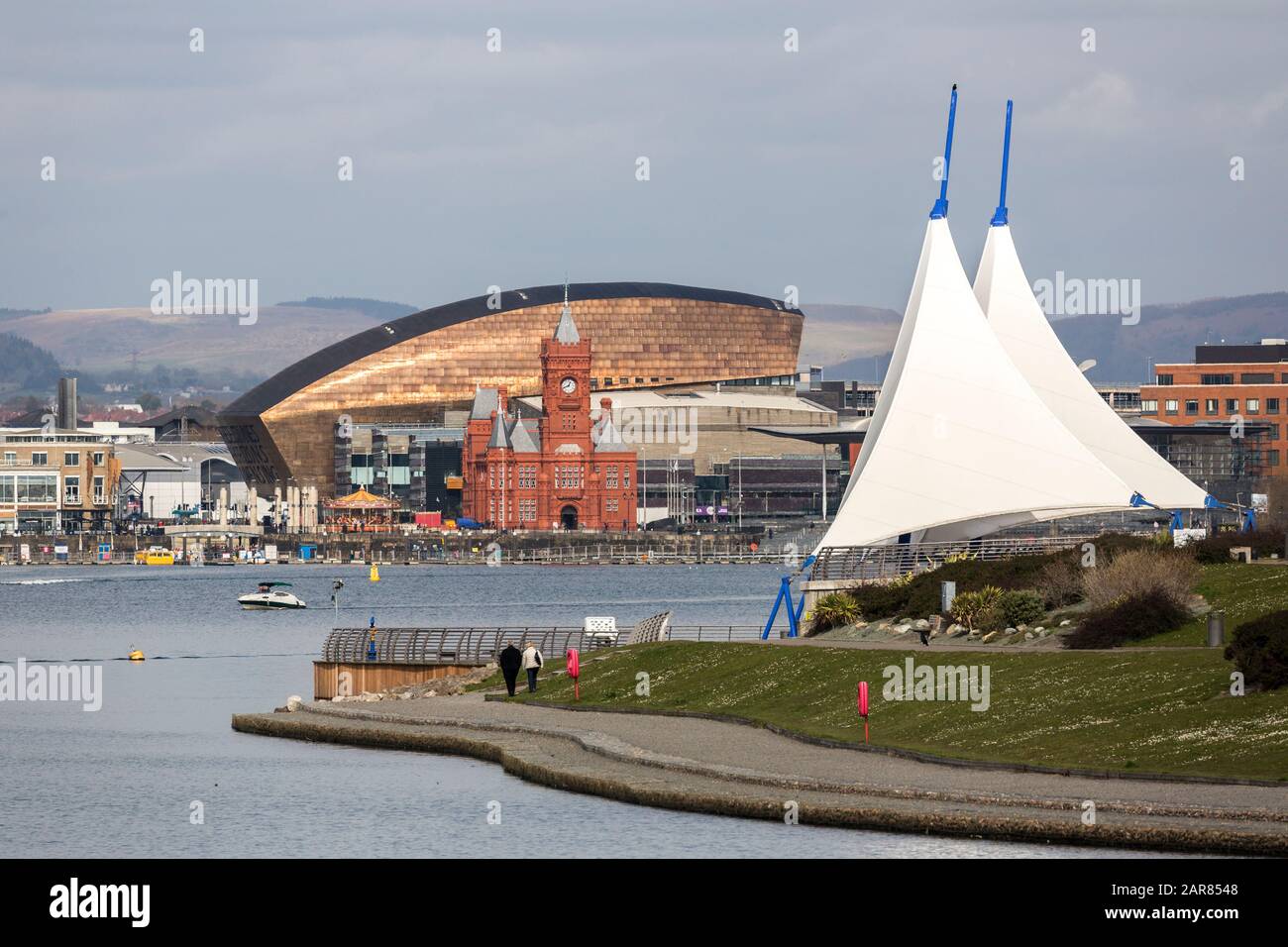 Pavillon mit Menschen, die auf der Barrage mit dem Pierhead Gebäude und dem Millennium Center, Cardiff Bay, Wales, Großbritannien spazieren gehen Stockfoto