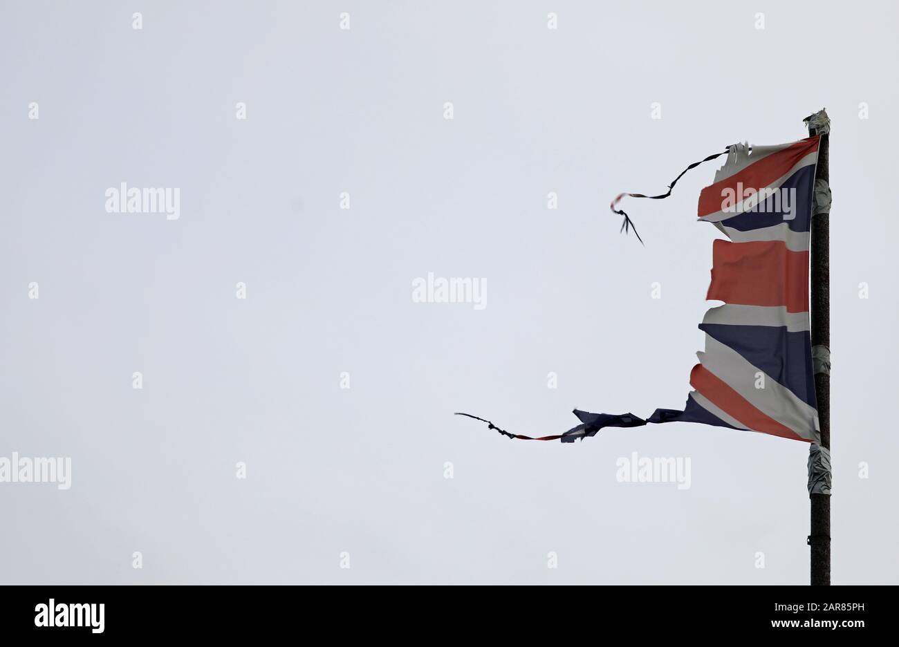 Union Jack, britische Flagge, zerfetzelt, gerissen, fliegen und flattern auf einem grauen Pfosten mit grauem Himmel könnte eine Katastrophe wie Krieg, Sturm oder Brexit illustrieren. Stockfoto