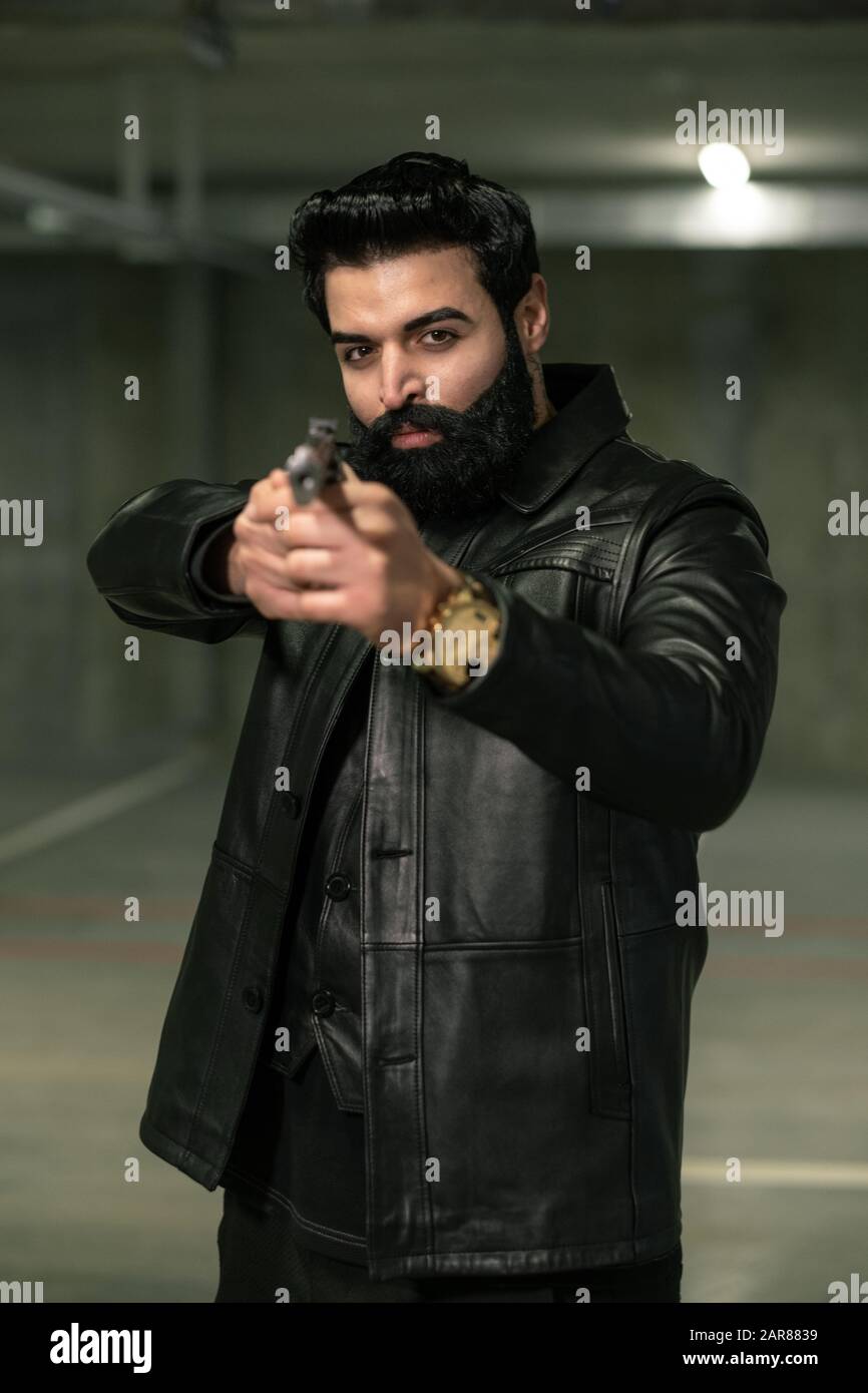 Assassin oder Terrorist in schwarzer Lederjacke, die die Handfeuerwaffe auf den Rivalen lenkt Stockfoto