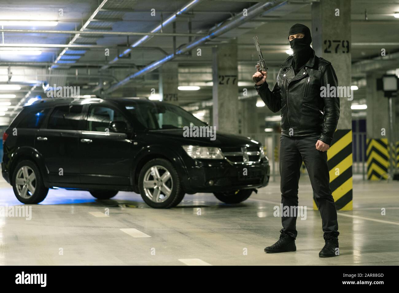 Terrorist oder Gangster in schwarzer Jacke und Balaklava auf dem Kopf, der Handfeuerwaffe hält Stockfoto