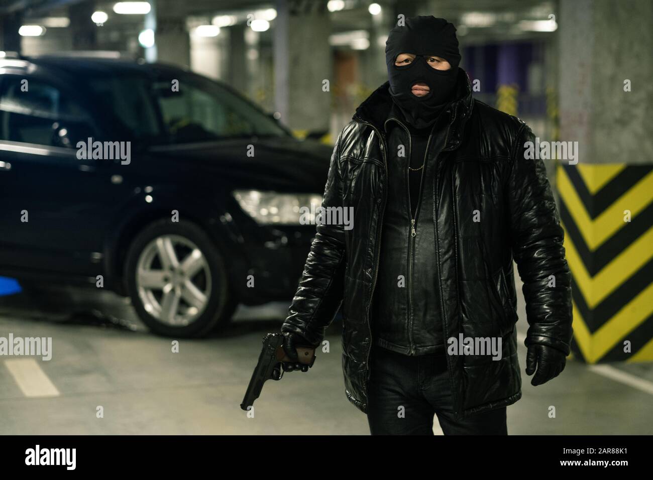 Terrorist oder Gangster in schwarzer Jacke, Handschuhen und Balaclava mit Handfeuerwaffe Stockfoto