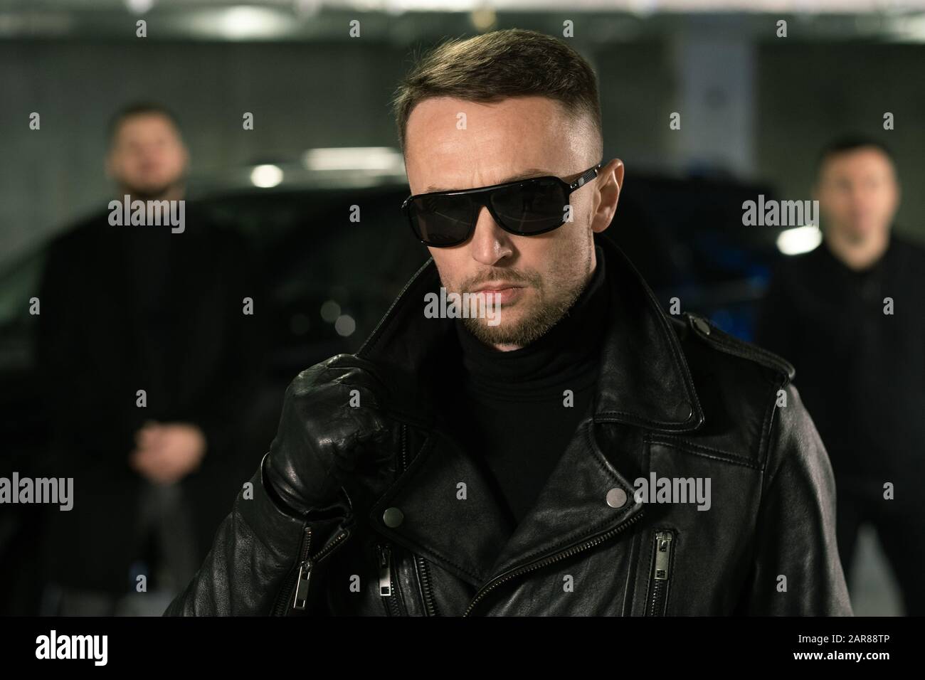 Spion oder Gangster in Sonnenbrille, schwarze Lederhandschuhe und Jacke Stockfoto