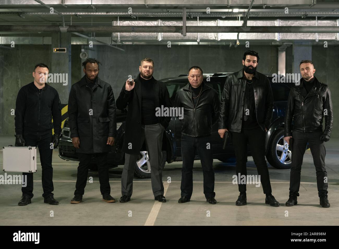 Reihe interkultureller bewaffneter Gangster oder Verbrecher in schwarzen Jacken und Jeans Stockfoto