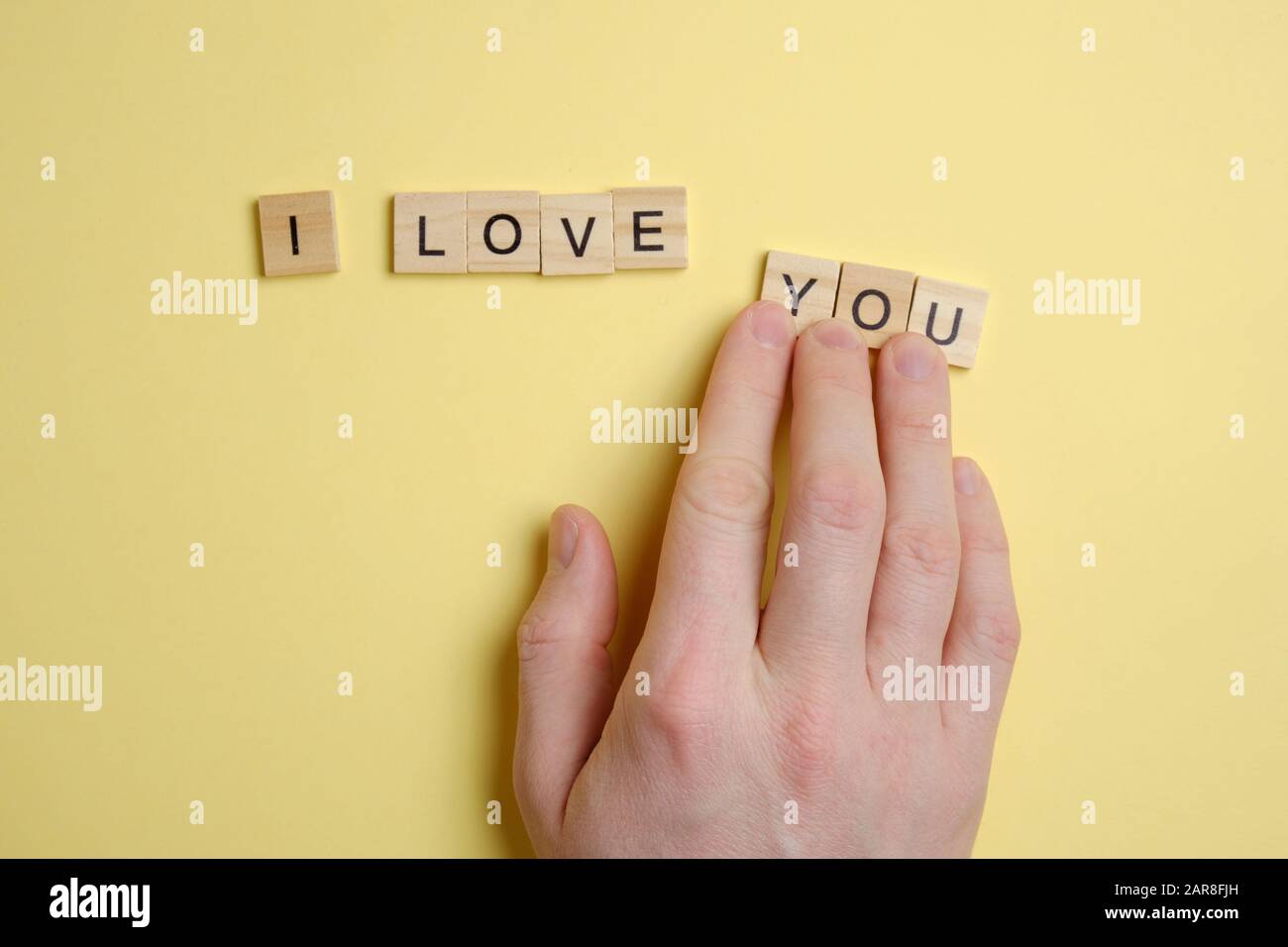 Das Wort - ich liebe dich - von Holzfeldern auf gelbem Hintergrund. Die Hand bewegt die Figuren. Draufsicht. Stockfoto