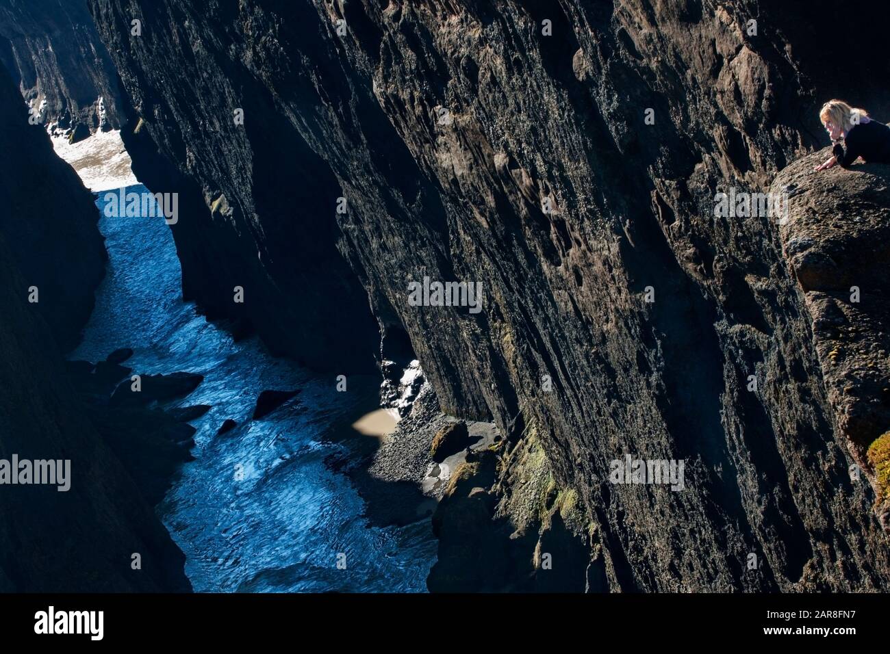 Die Touristin lehnt sich an einen Felsen mit Blick auf einen Fluss, der durch einen schmalen Canyon in Nordisland führt, den Hafrahvammaglijufrum Staudamm, Island, Europa Stockfoto