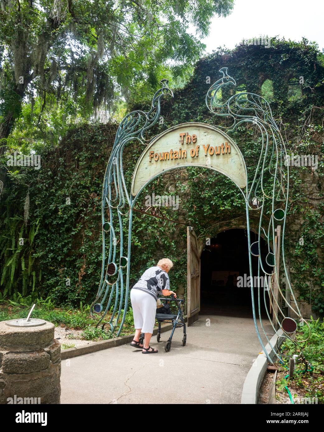 Die kacuasische Frau im hohen Alter lehnt sich an einen Wanderer, um den mit Weinstock bedeckten Eingang zum Jungbrunnen in St. Augustine, Florida, USA, zu betreten Stockfoto