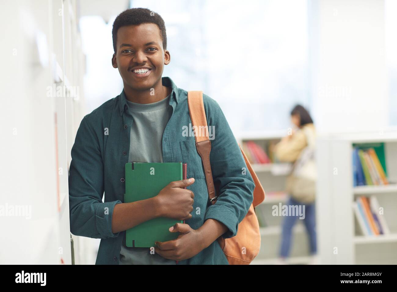 Taille hoch Porträt von afroamerikanischen Studenten Blick auf die Kamera und lächeln, während sie in Regalen in der College-Bibliothek posieren, Kopierraum Stockfoto