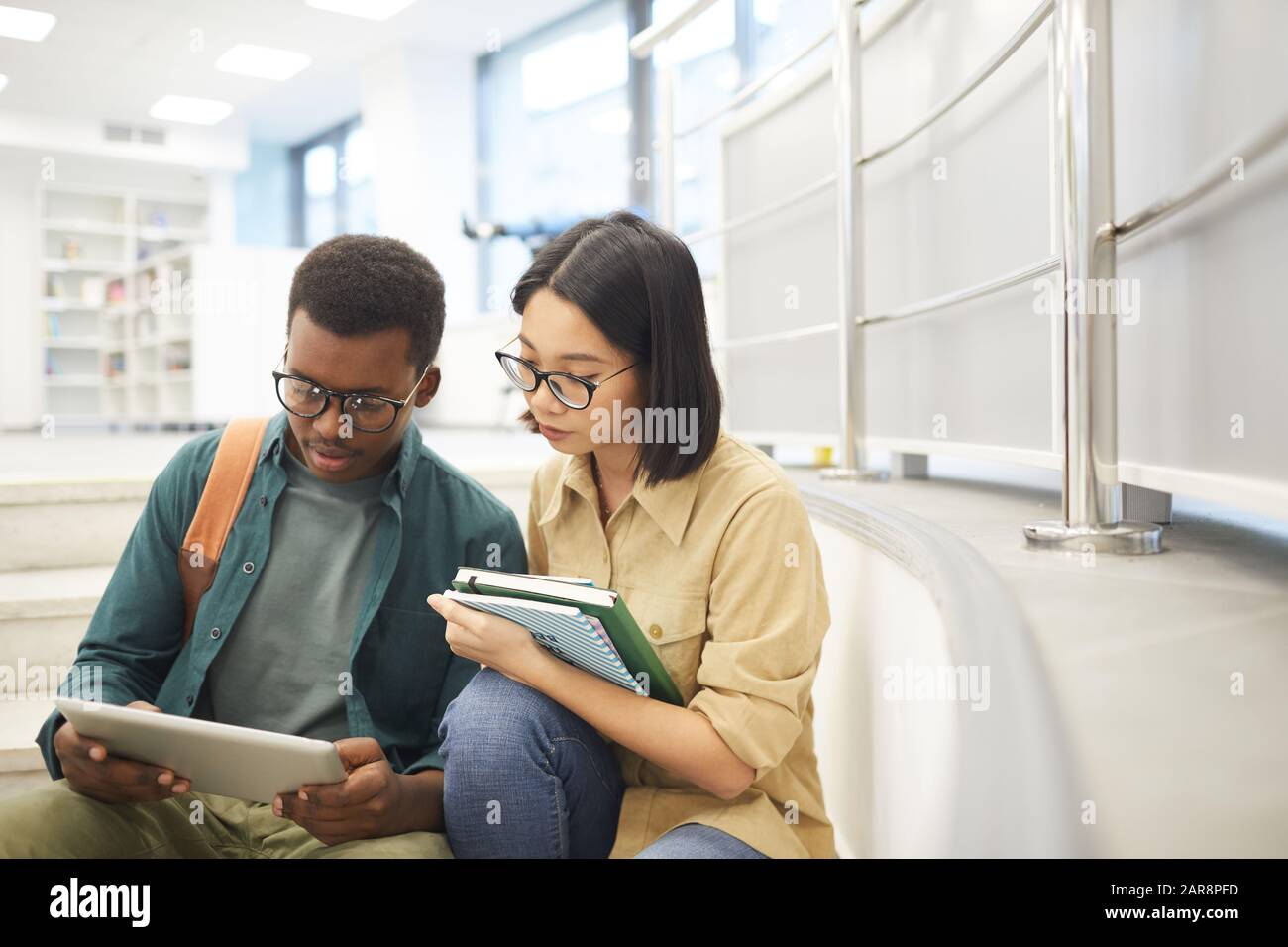 Porträt zweier internationaler Studenten, die gemeinsam Bücher lesen, während sie an Projekten in der modernen Hochschulbibliothek arbeiten, Kopierraum Stockfoto