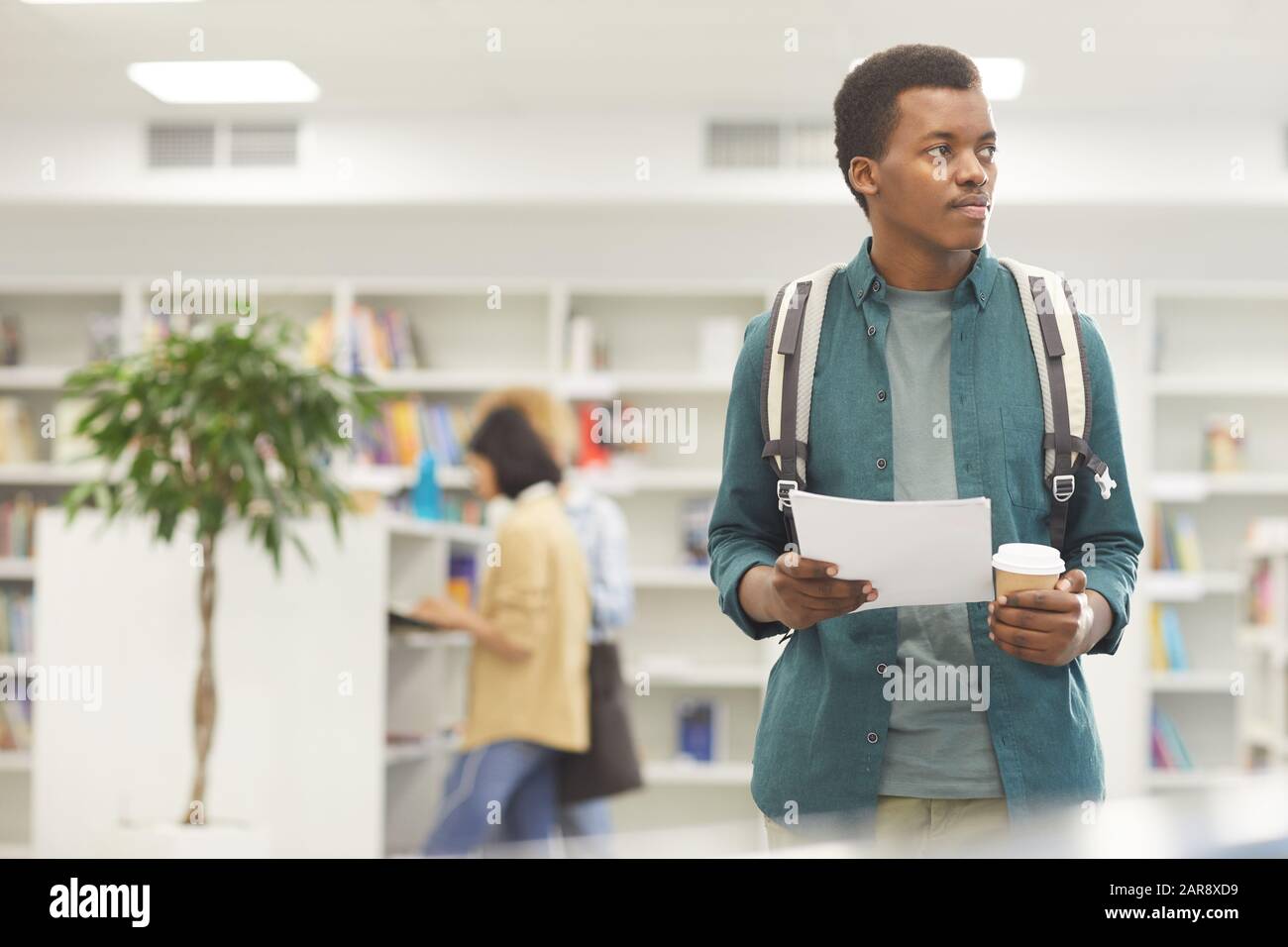 Taillen-Up-Porträt von afroamerikanischen Studenten, die in der College-Bibliothek eine Tasse Kaffee halten, Platz für Kopien Stockfoto