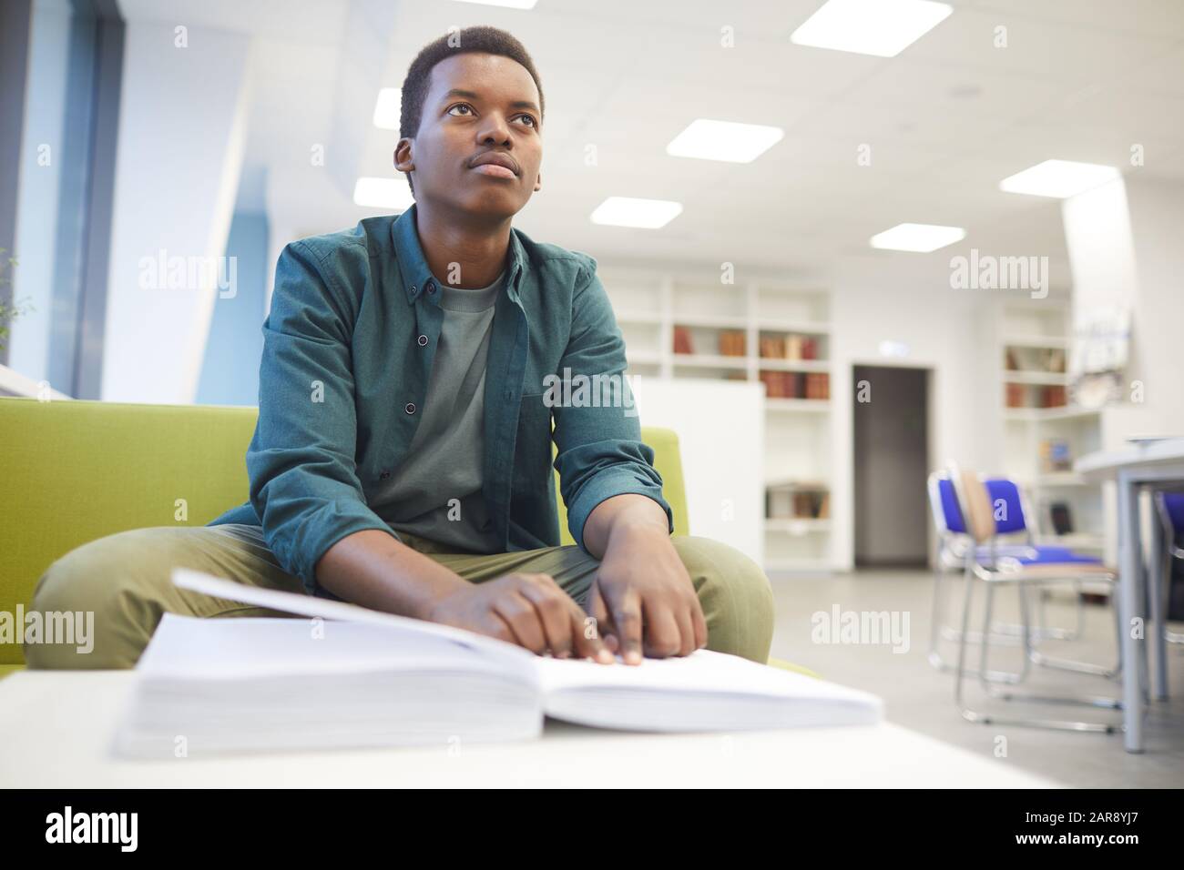 Portrait des jungen afroamerikanischen Mannes, der Braille liest, während er in der Schulbibliothek studiert, kopiere Raum Stockfoto