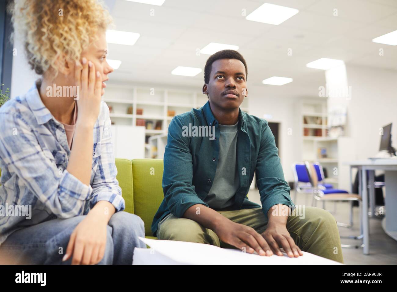 Portrait des jungen afroamerikanischen Mannes, der Braille liest, während er mit einem sehenden Freund in der Schulbibliothek studiert, kopiere Raum Stockfoto