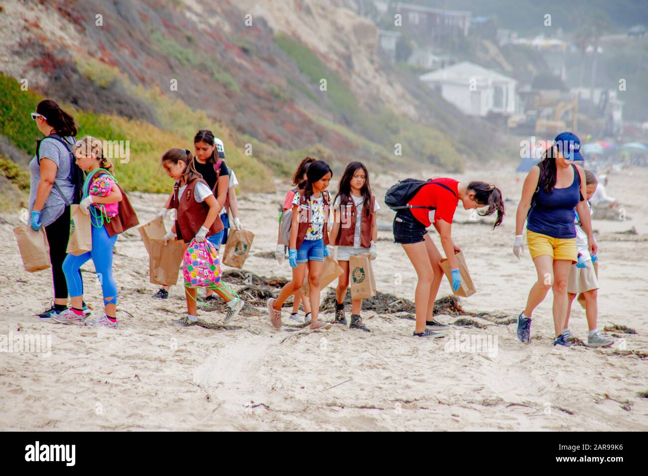 In ihren Brownie Girl Scout Westen und Gummihandschuhen und Trashtaschen tragen Töchter ihre Mütter auf der Suche nach der Weigerung, sich am Ufer in Laguna Beach, CA zu sammeln. Stockfoto