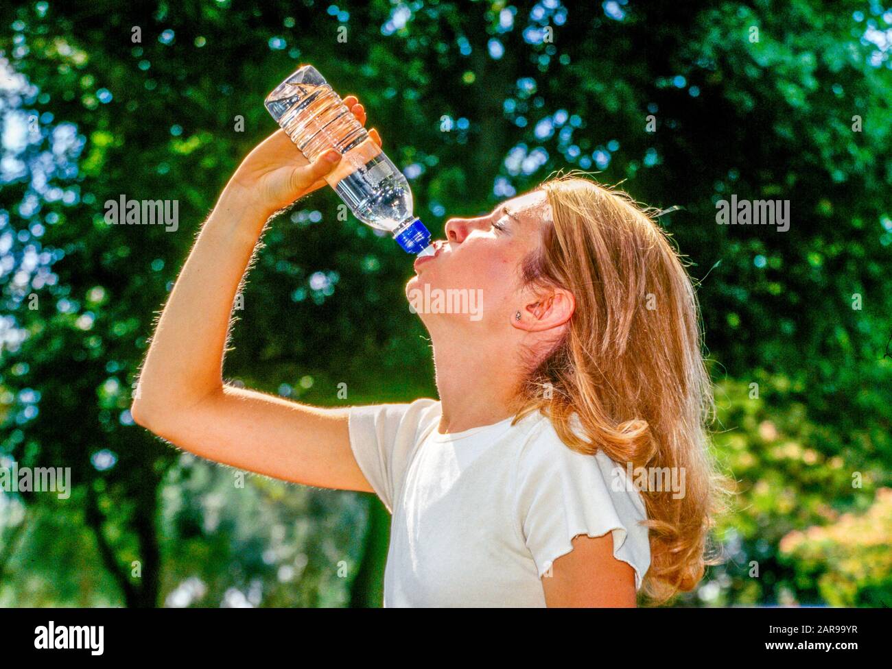 Eine blonde junge Erwachsene Joggerin macht eine Pause vom laufen, um ein erfrischendes Getränk aus einer Flasche Wasser in einem Long Beach, CA, City Park MODEL RELEASE zu sich zu nehmen Stockfoto