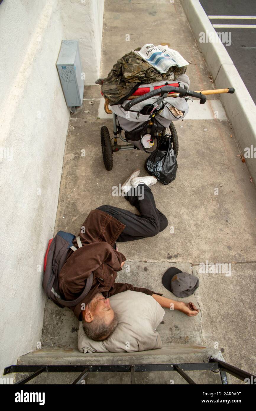 Sein weltlicher Besitz auf einem Gepäckwagen schläft ein Obdachloser im Freien in einer Gasse hinter einer Kirche in Costa Mesa, Kalifornien. Stockfoto