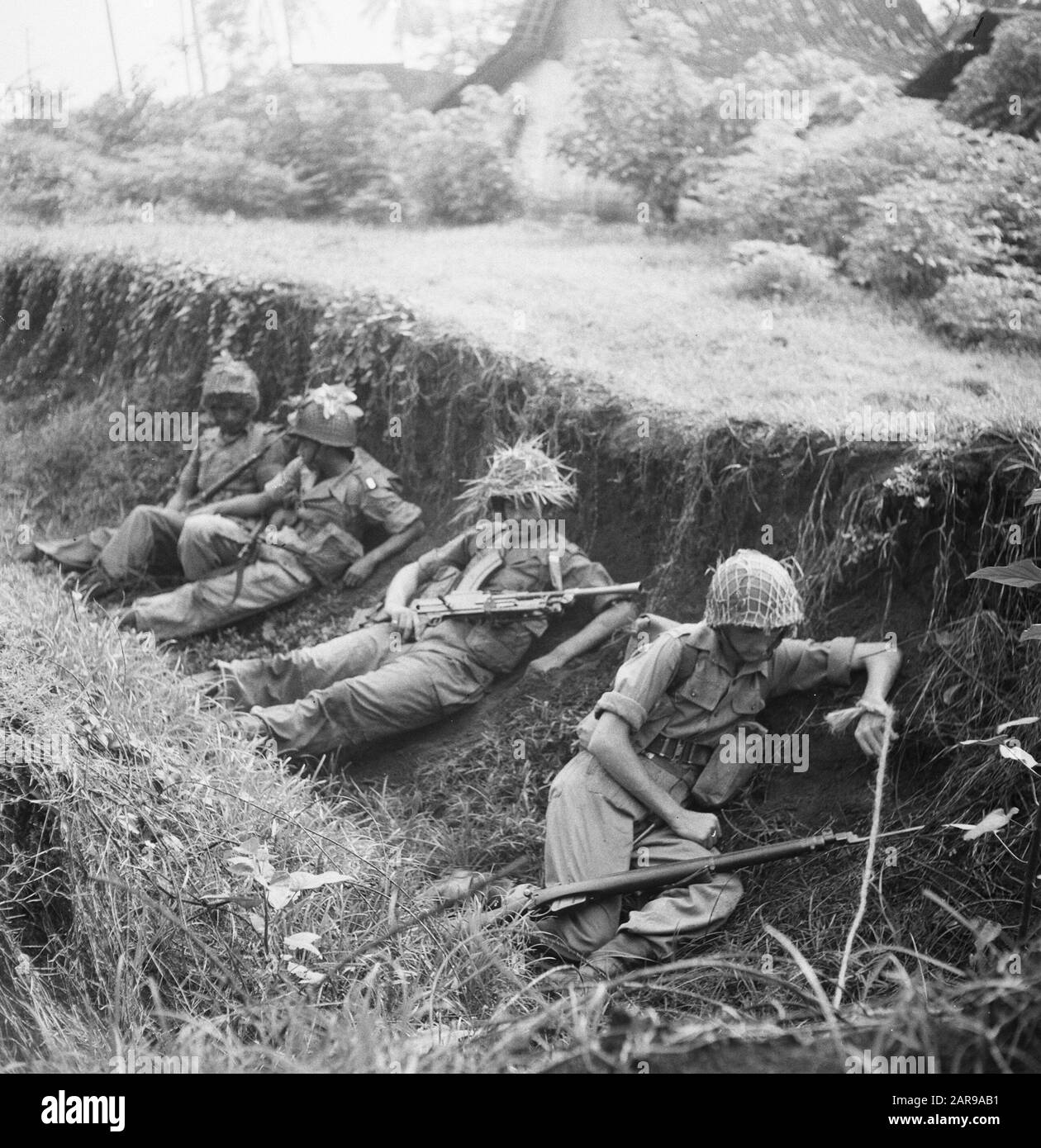 V.P.T.L. [Vier Soldaten liegen versteckt in einem Graben] [Nehmen Sie eine einfache Position in einem Hinterhalt... es kann eine lange Zeit dauern. Allerdings Waffen IM man und das Warnseil am Handgelenk am Mann am Flügel!!!] Anmerkung: V.P.T.L. = Voraussetzung für die Ausübung der Politischen Polizeiaufgabe der Armee (Aktion gegen Guerillakämpfer). Diese Regel der KNIL geht auf das Jahr 1928 zurück, erschien 1936 und wurde 1945 geändert und ergänzt und 1946 wieder veröffentlicht, nun speziell für die KL. Die Fotoserie wurde für die Broschürenkenntnisse der V.P.T. L., eine Frage des Lebens oder Todes/Mengetahoei Akan V.P.T. verwendet Stockfoto