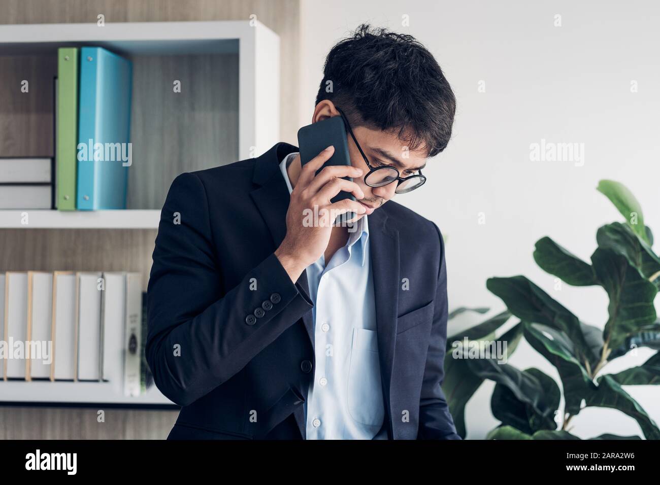 Junge asiatische Geschäftsmann tragen Anzug sprechen auf mobile und siehe Schreibarbeit am Schreibtisch Tisch in modernen Büro. Kontakt mit Kunden Konzept Stockfoto