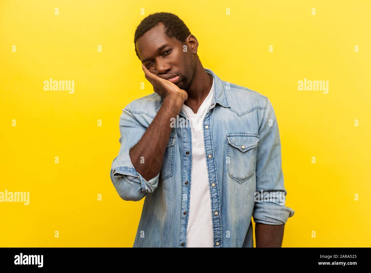 Mir ist langweilig. Porträt eines müden, uneigennützigen Mannes mit Jeans-Hemd, das den Kopf an der Hand hält, mit schläfriger, gleichartiger Ausdrucksweise, Faulheit aussieht. Indoo Stockfoto