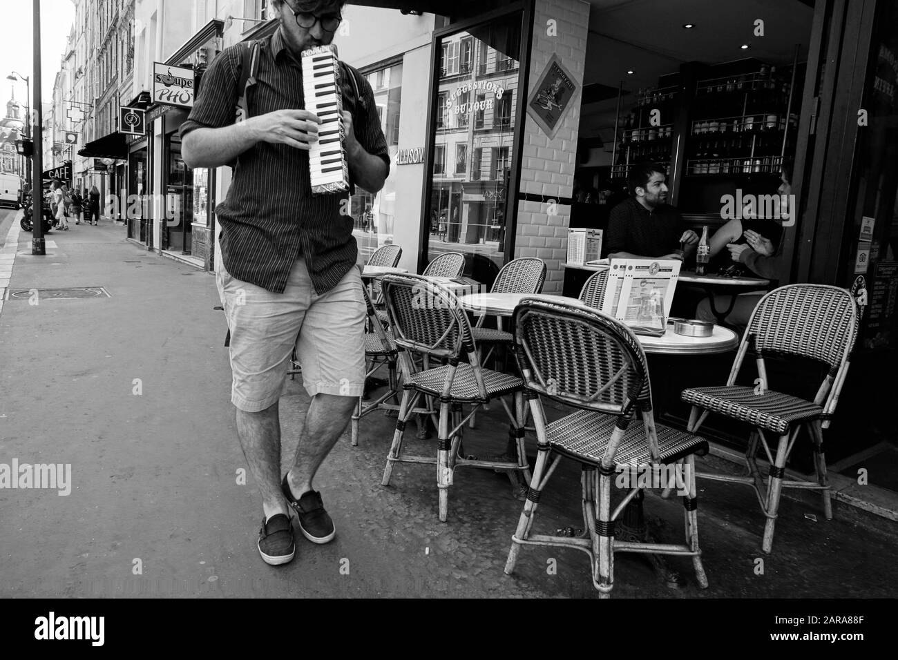 Mann, der auf der Tastatur Mundharmonika, Mundorgel, Café auf dem Straßenbelag, Rue Saint Antoine, Paris, Frankreich, Europa spielt Stockfoto
