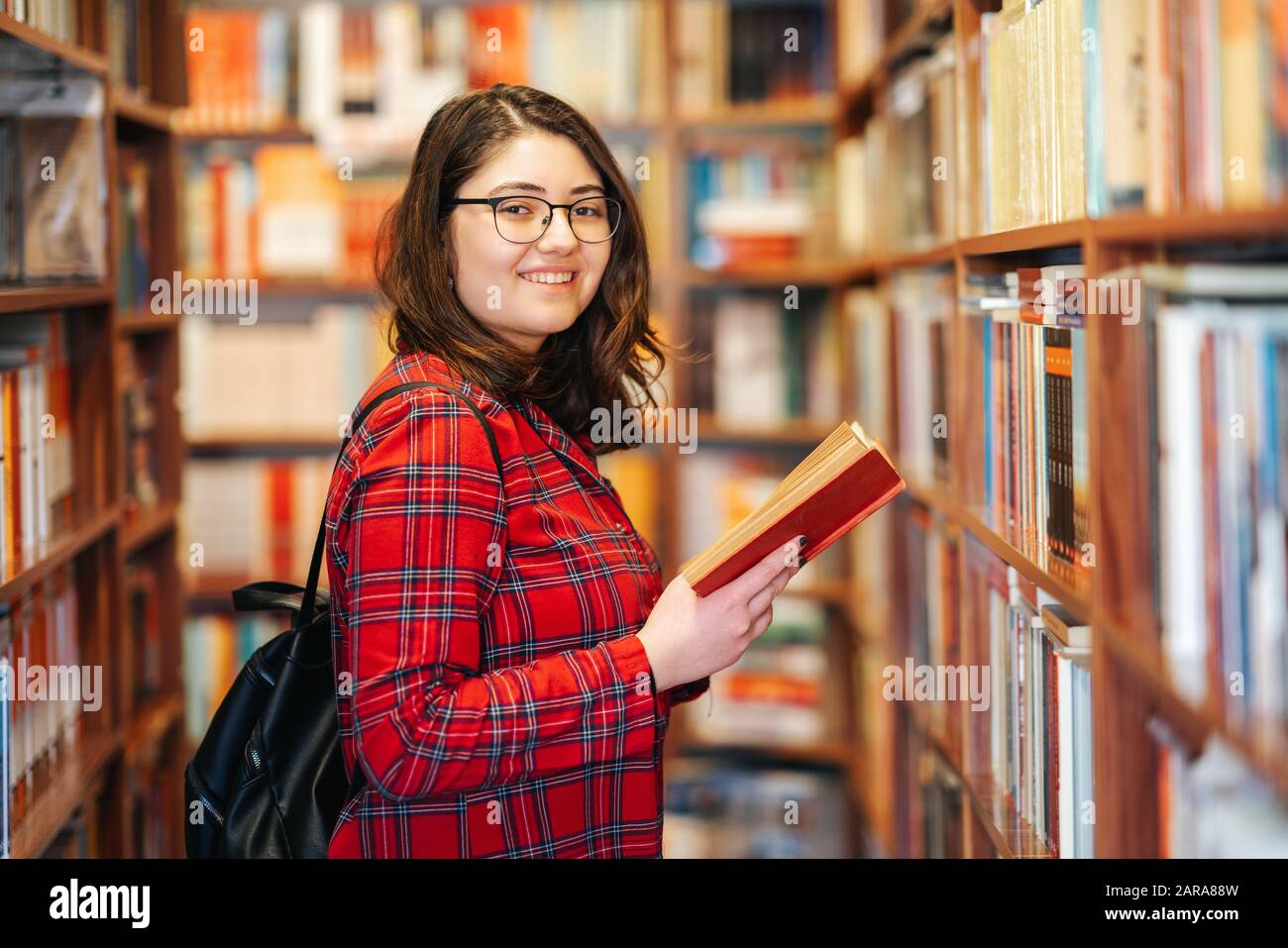 Intellektuelles Teenager-Mädchen wählt Bücher aus und wählt sie mit einem fröhlichen Lächeln aus einer Bibliothek oder einem Buchladen Stockfoto