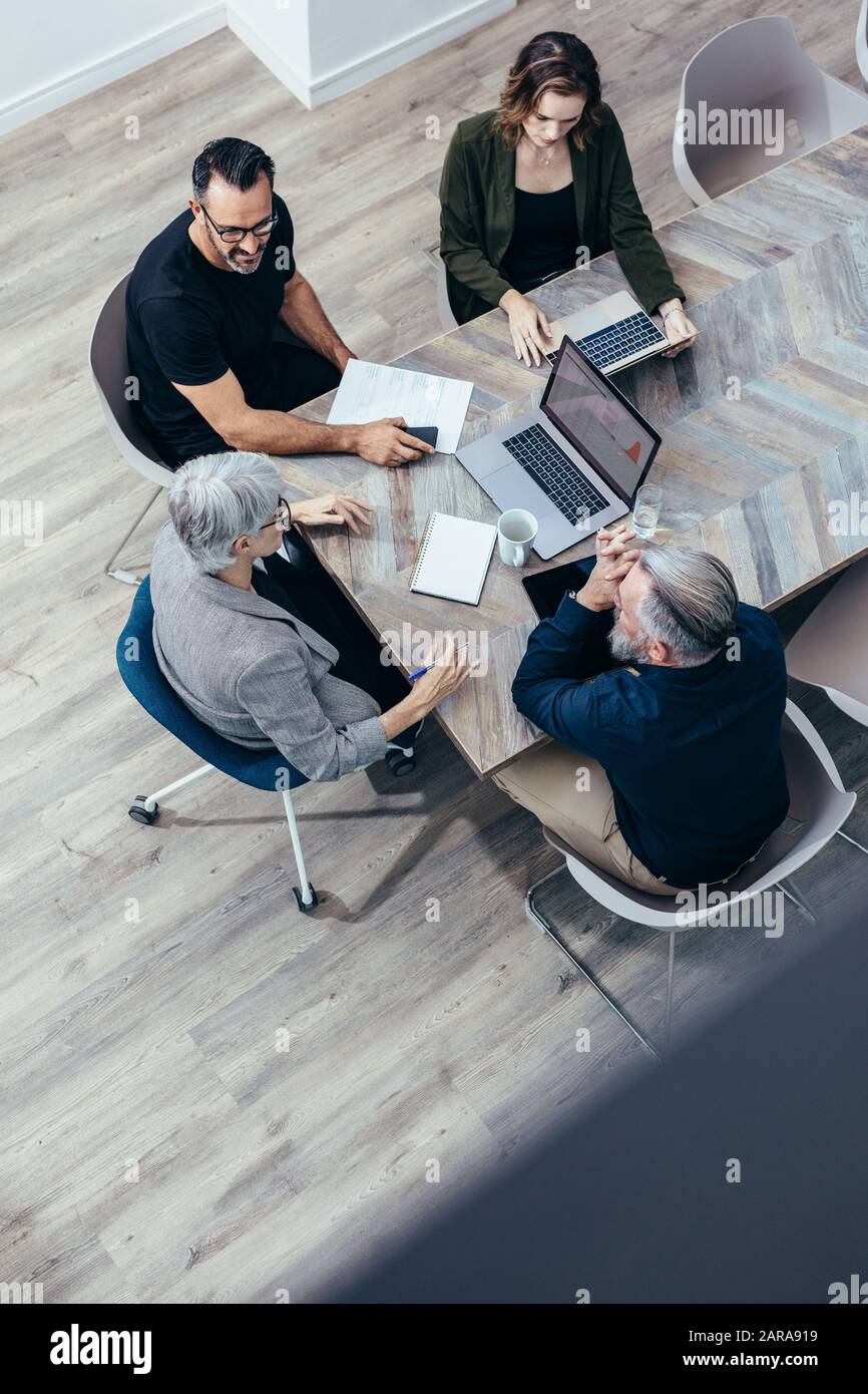 Draufsicht über das Business-Team, das um einen Tisch sitzt und diskutiert. Eine hochwinkelige Ansicht von Geschäftsleuten, die eine Brainstorming-Sitzung haben. Stockfoto