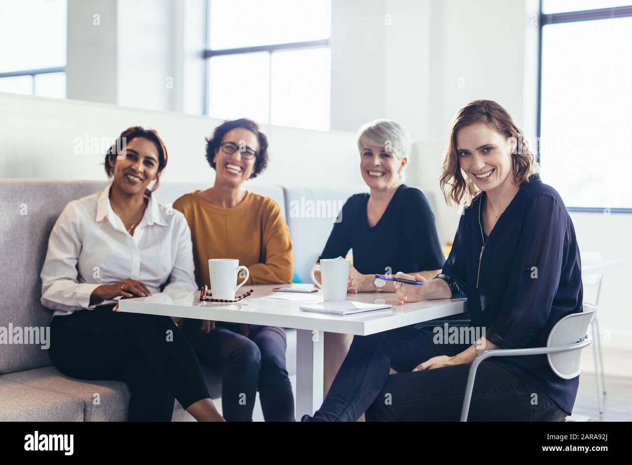Vier Geschäftsfrauen sitzen am Tisch und schauen auf die Kamera. Team von weiblichen Business-Profis. Stockfoto