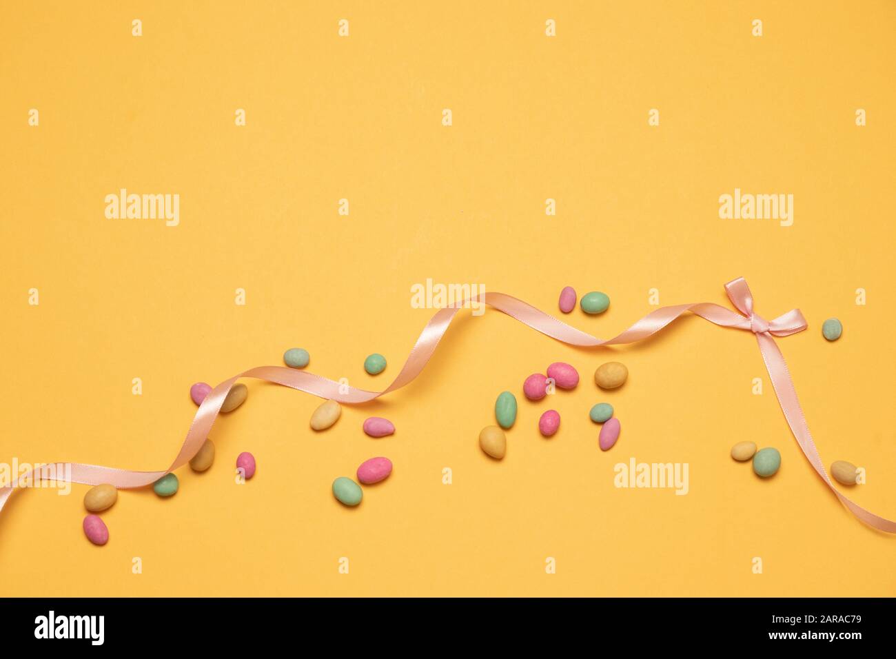 Farbige Zuckerbonbohnen und Seidenbandbogen auf gelbem Hintergrund mit Copyspace. Grußkarte für frohe ostern, Geburtstag, Muttertag, Rabattbanner Stockfoto