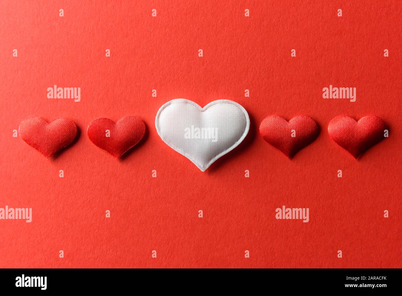 Rot-weiße Textilherzen auf rotem Papier. Valentinstag Hintergrund, kreative Textur und Liebeskonzept Stockfoto