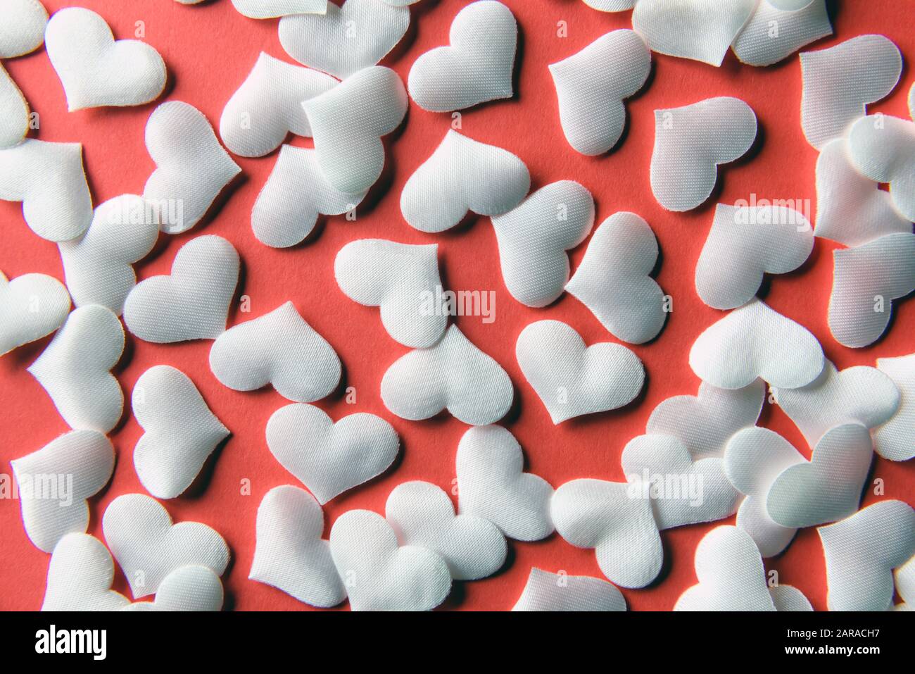 Weiße Textilherzen auf rotem Papier. Valentinstag Hintergrund, kreative Textur und Liebeskonzept Stockfoto