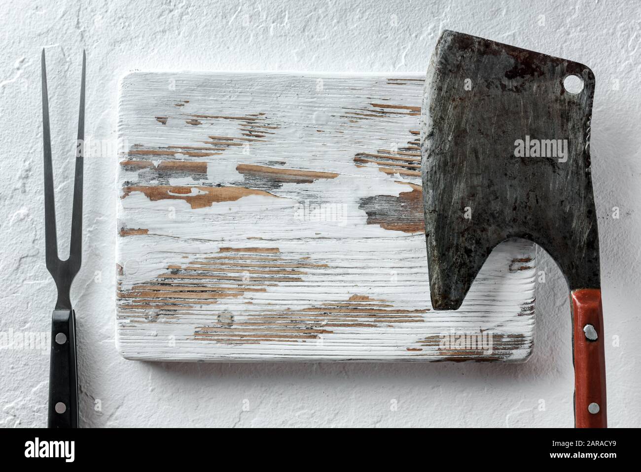 Alte rustikale Metallklumpen und Fleischmesser auf weißem Holzbrett auf rustikalem Betontisch. Lebensmittelfotografie. Menü-Mockup Stockfoto