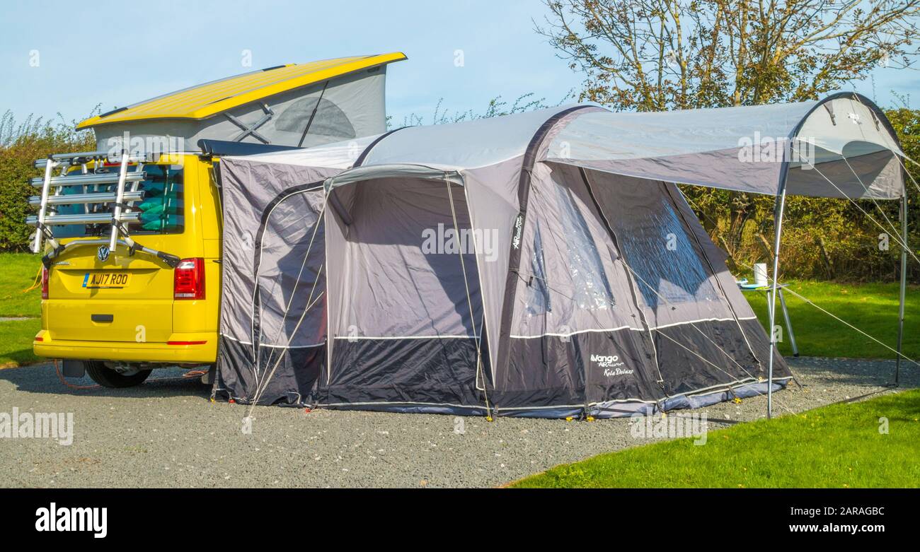 Ein hellgelber Kampervan mit angeschlossenem Fahrradträger, aufgehobenem Popup-Dach und einem angebauten Zelt/Markise auf einem Zeltplatz. England, Großbritannien. Stockfoto