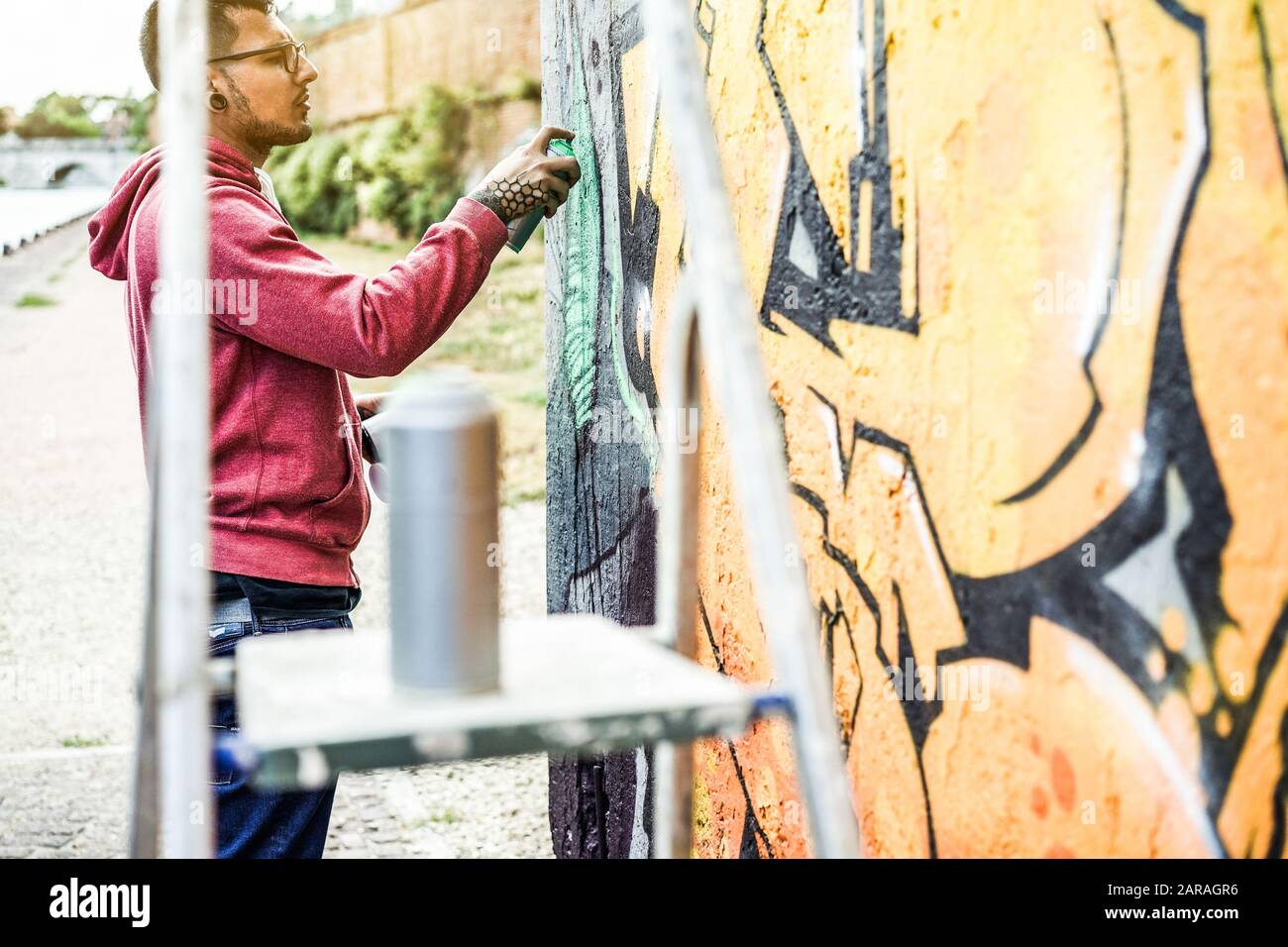 Tätowier-Graffiti-Schriftstellergemälde mit Farbspray an der Wand - Zeitgenössischer Künstler bei der Arbeit - urbaner Lebensstil, Street-Art-Konzept - Fokus auf sein Gesicht an Stockfoto
