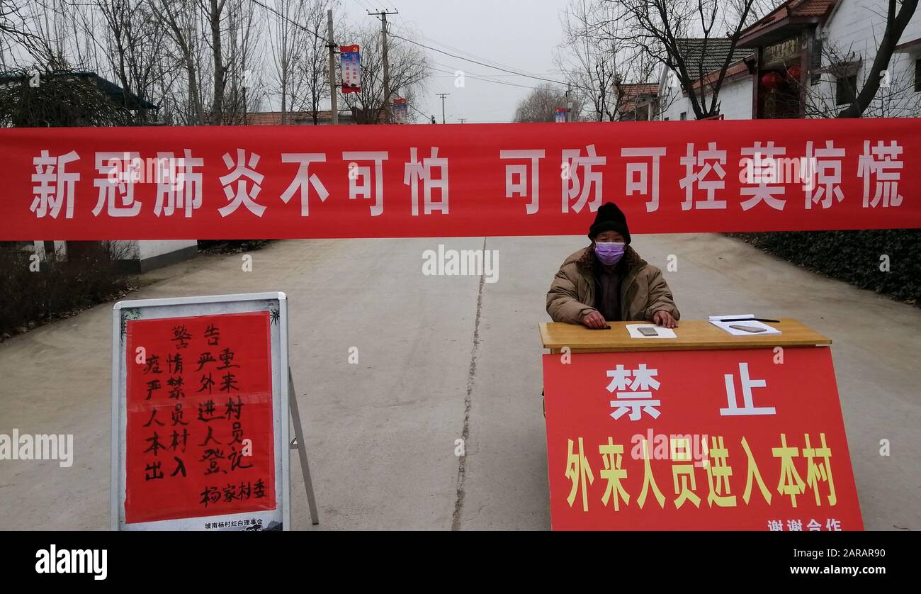 Ein chinesischer Inspektor sitzt vor einem Banner mit Sprüchen, die sagen: "Das neue Coronavirus und die Pneumonie sind nicht unheimlich. Es ist vermeidbar und kontrollierbar. Stockfoto