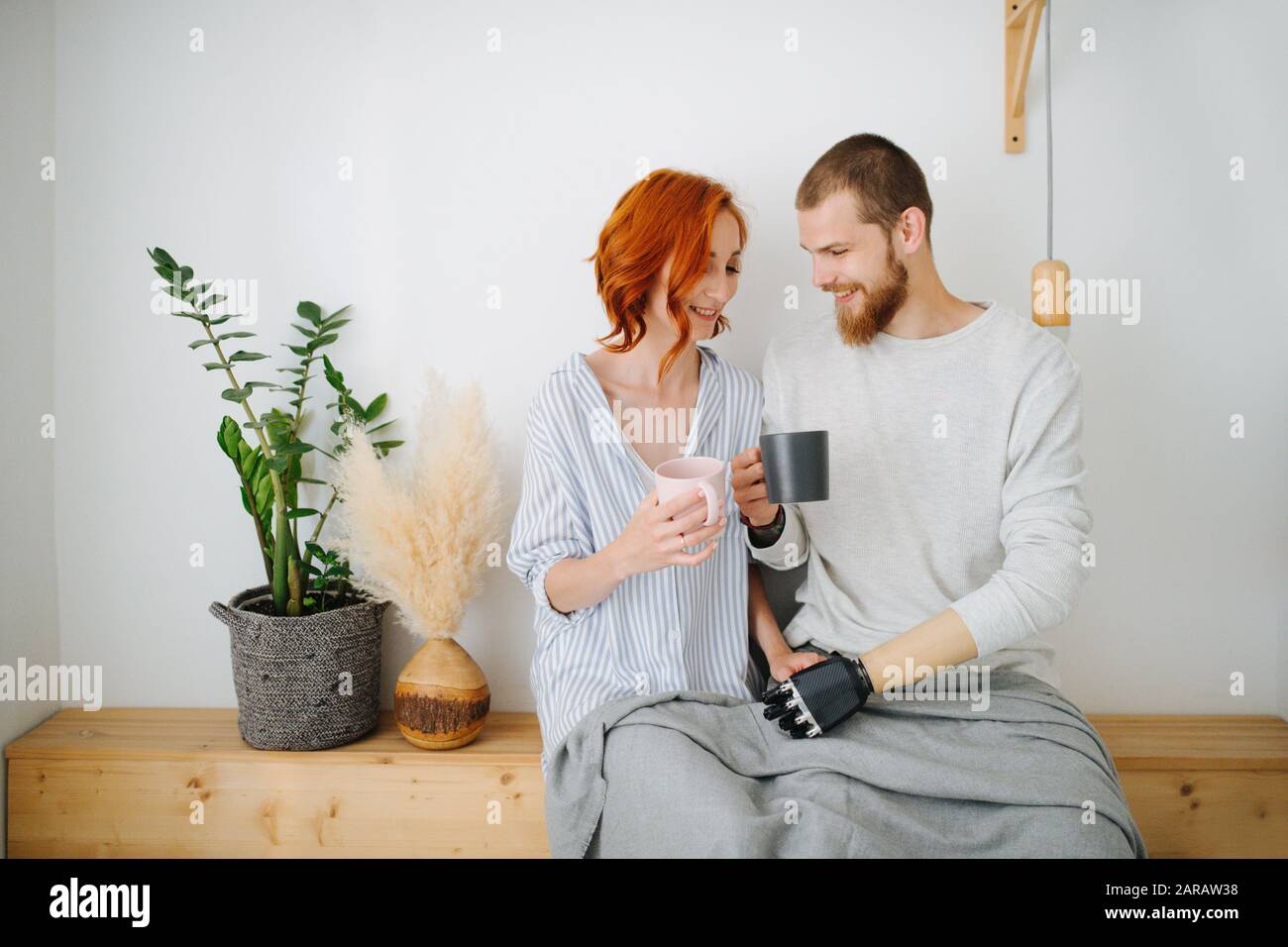 Glücklicher Ehemann und Frau sitzen zusammen auf einem Regal und trinken zu Hause Kaffee. Stockfoto